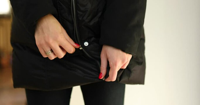 Woman's hand unfasten the zipper on a black jacket