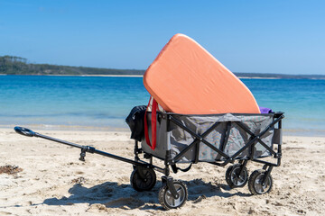 Outdoor beach cart wagon on a sandy beach near the ocean. Family vacation holidays mock up - obrazy, fototapety, plakaty