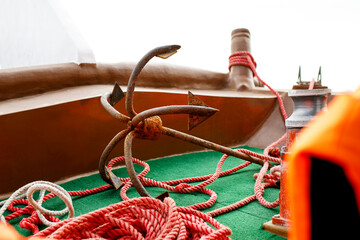 Large rusty anchor on an old fishing boat tied with a red rope to the boat, selective focus