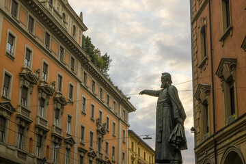 Naklejka premium the Statue of Ugo Bassi in the Ugo Bassi street across the orange buildings and sky in Bologna, Italy