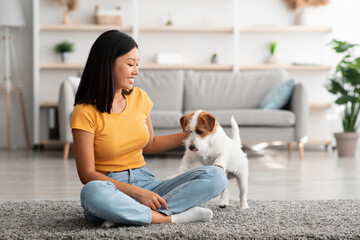 Pretty asian woman enjoying time with puppy at home