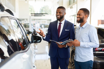Black Salesman Advertising New Automobile To Male Customer In Car Dealership Center