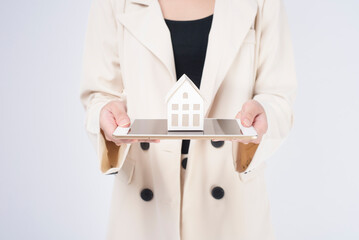 Young beautiful woman in suit holding small model house over white background studio