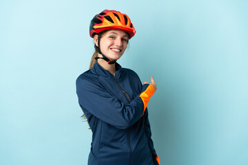 Young cyclist woman isolated on blue background pointing back