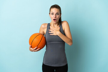 Young woman playing basketball isolated on blue background surprised and shocked while looking right