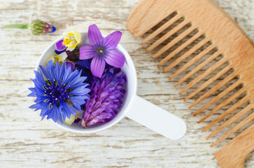 Obraz na płótnie Canvas Plastic scoop with various field flowers and hairbrush. Ingredients of natural cosmetic. Organic hair care, homemade beauty treatment and spa concept.