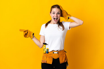 Young electrician woman isolated on yellow background surprised and pointing finger to the side