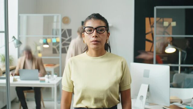 Time lapse shot of beautiful Hispanic businesswoman standing in open office during workday and looking at camera