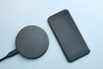 High angle view of modern smartphone with dimmed display next to round wireless charger on light...