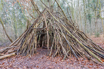 Small hut made of tree branches in the Leudal nature reserve, bare trees in the misty and blurred background, Midden-Limburg in the Netherlands. Shelter concepts for survival