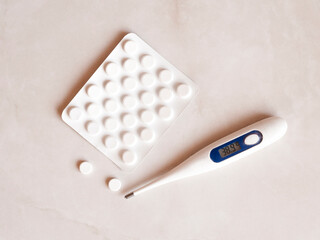 Tablets and a thermometer on a light background. Top view