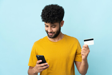 Young Moroccan man isolated on blue background buying with the mobile with a credit card