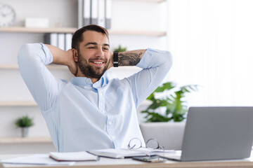 Smiling mature european male with beard take a break from work at laptop in office or living room