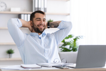 Obraz premium Smiling mature european male with beard take a break from work at laptop in office or living room