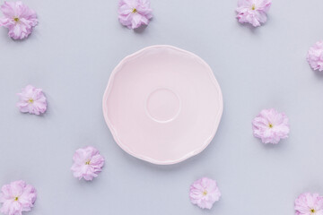 Empty small pink plate or saucer and fresh spring cherry blossom flowers on pastel gray background. Tea party, drinking coffee or dessert recipe concept. Top view, flat lay, copy space