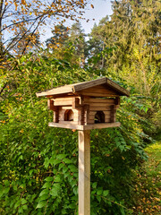 Wooden bird feeder in front of bushes