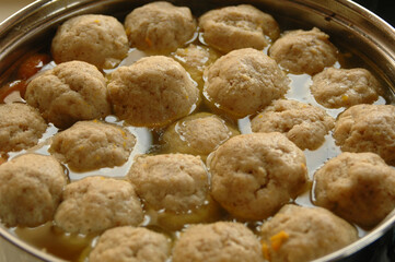 Large pot of chicken soup with matzah balls floating on the surface. 