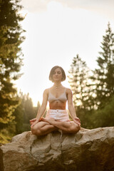 woman in white shorts making yoga pose on the stone, sunset light
