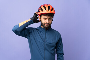 Young Moroccan cyclist man isolated on purple background having doubts - obrazy, fototapety, plakaty