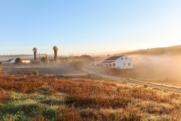 View of typical Alentejo landscape with Portuguese village in morning fog an rising sun at the Rota Vicentina hiking trail near Carrascalinho, Aljezur, Algarve and Alentejo area in Portugal