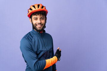 Young Moroccan cyclist man isolated on purple background pointing back
