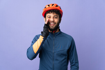 Young Moroccan cyclist man isolated on purple background shouting with mouth wide open - obrazy, fototapety, plakaty