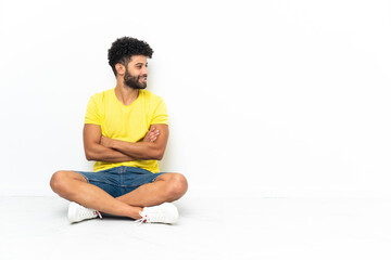 Young Moroccan handsome man sitting on the floor over isolated background looking side