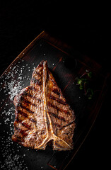 Grilled T-bone Steak on bones on wooden plate on bkack background