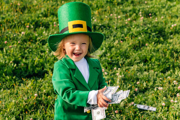 Funny little girl dressed as a leprechaun, he holds money in his hands and laughs. A child on a...
