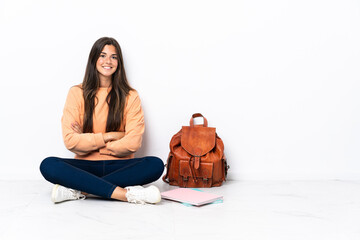 Young student brazilian woman sitting on the floor keeping the arms crossed in frontal position