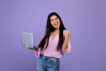 Entertainment and work online. Happy armenian lady holding laptop and expressing emotions of success, violet background