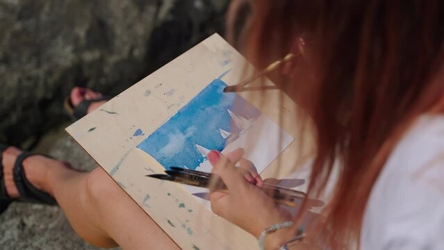 Female artist painting seascape in open air