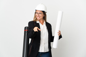 Middle age architect woman with helmet and holding blueprints over isolated background pointing front with happy expression