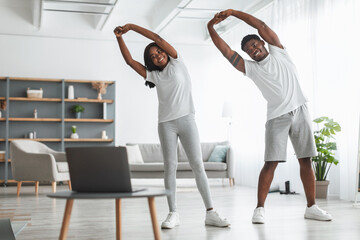 Young black couple doing side bend exercise using pc