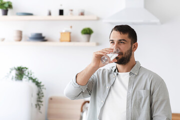 Attractive middle aged european male in casual drinking water from glass on minimalist kitchen...
