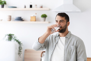 Attractive middle aged european male in casual drinking water from glass on minimalist kitchen interior