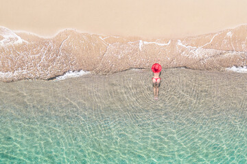 Top view. Young beautiful woman in a red hat and bikini lying and sunbathe in sea water on the sand...