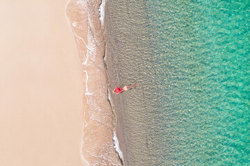 Top view. Young beautiful naked woman in a red hat lying and sunbathe in sea water on sand beach....
