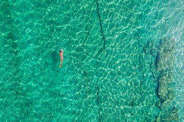 Alone naked nudist man dives in flippers, snorkeling mask and tube swimming in sea, ocean turquoise clear water. Top view. Aerial, drone, copter view.