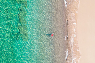 Top, aerial view. Young beautiful woman in a red hat and bikini walking, swimming, sunbathe in sea water on the sand beach. Drone, copter photo. Summer vacation. View from above.