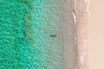 Top view. Young beautiful woman in red hat standing and sunbathe in sea water. Drone, copter photo. Summer vacation. View from above.