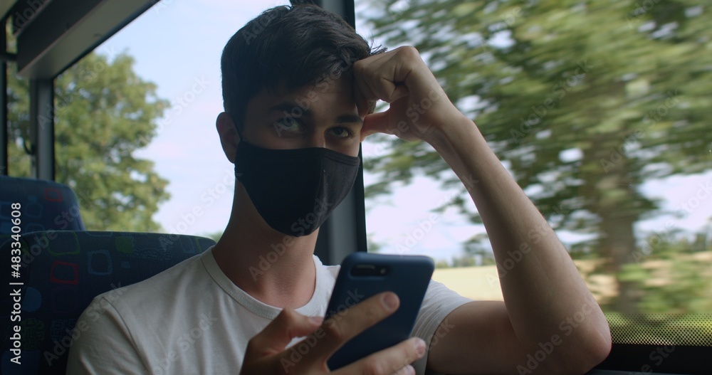 Poster a man in a black mask uses a phone near the bus window in motion. look at the screen along the route