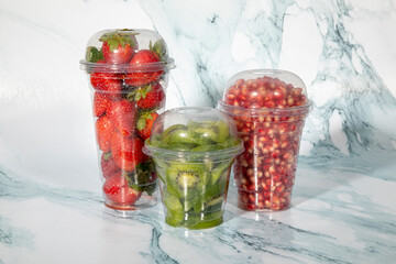 Tomatoes, cucumbers, carrots in plastic cups. Plastic cup with background. Plastic cup and vegetables. Snack serving containers. Full plastic cup on colored background. Food in a clear glass