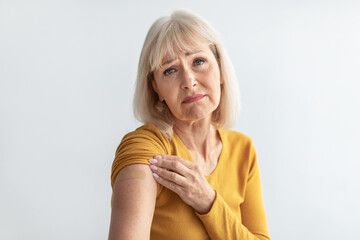 Unhappy Senior Woman Showing Vaccinated Arm With Plaster, Gray Background