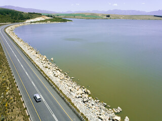 Aerial of car driving across a dam wall