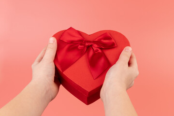 Red box in shape of heart. Gift box for Valentine's Day in the kids hands. Isolated on pink background.