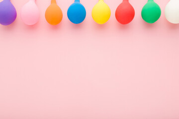 Row of colorful balloons on light pink table background. Pastel color. Closeup. Empty place for inspirational, positive text, lovely quote or sayings for good mood. Top down view.