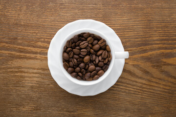 White cup of black coffee with brown beans on dark wooden table background. Closeup. Top down view.