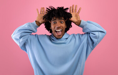 Cool African American teen guy making silly gesture with his hands, grimacing and having fun on pink studio background - obrazy, fototapety, plakaty
