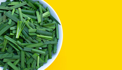 Fresh Chinese Chive leaves in white bowl on yellow background.